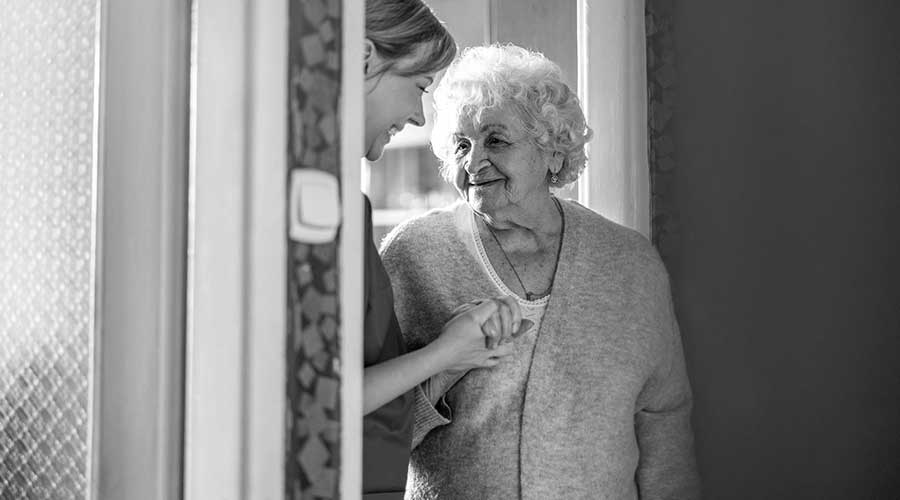 Pflegerin hält lächelnd Hand von Seniorin